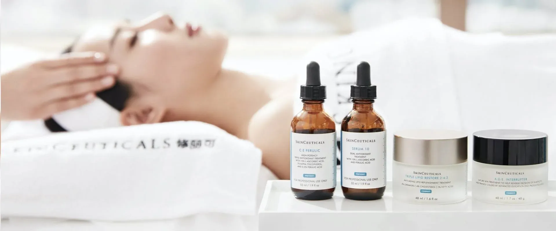 A woman is receiving a facial treatment while several SkinCeuticals skincare products are displayed.