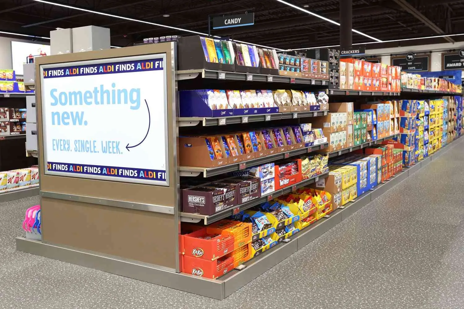 A candy aisle inside an ALDI store featuring shelves of chocolates and snacks with a sign promoting "Something new every single week".