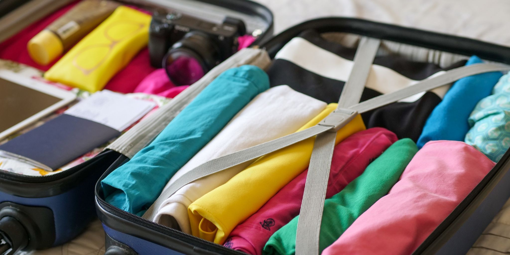 A blue luggage packed with colorful pieces of clothing.