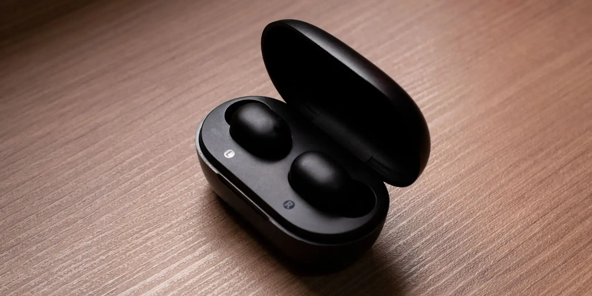 Wireless earbuds in a case on a wooden table.