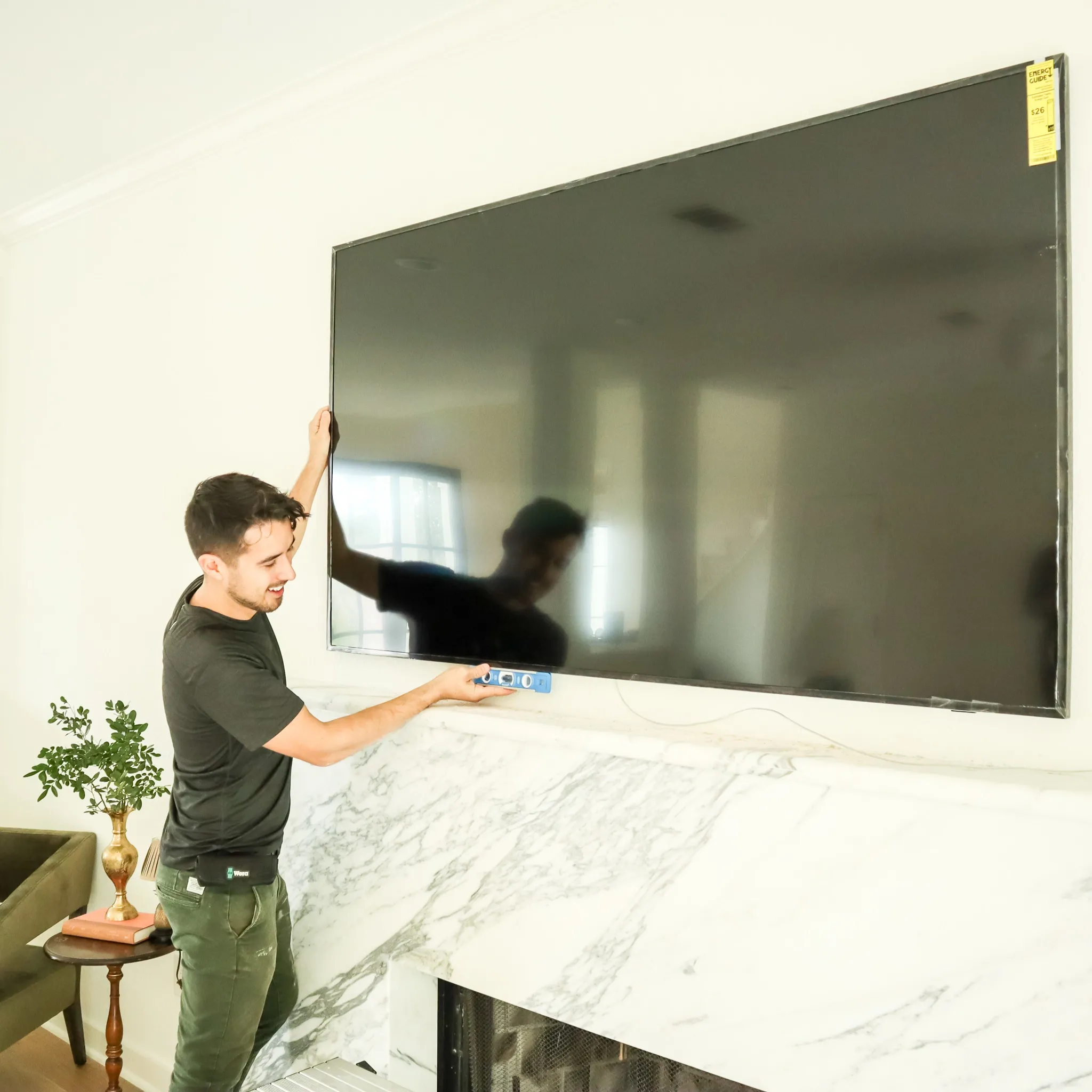 A man is mounting a TV above a marble fireplace.