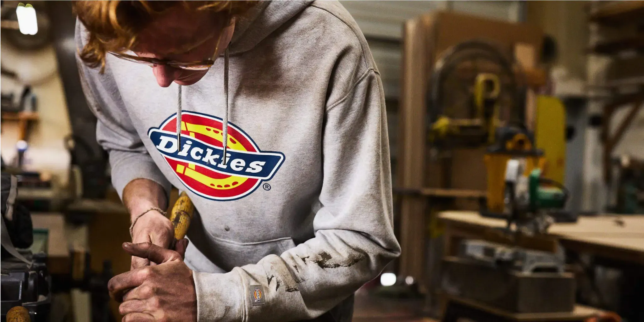 A person in a gray Dickies hoodie working in a workshop