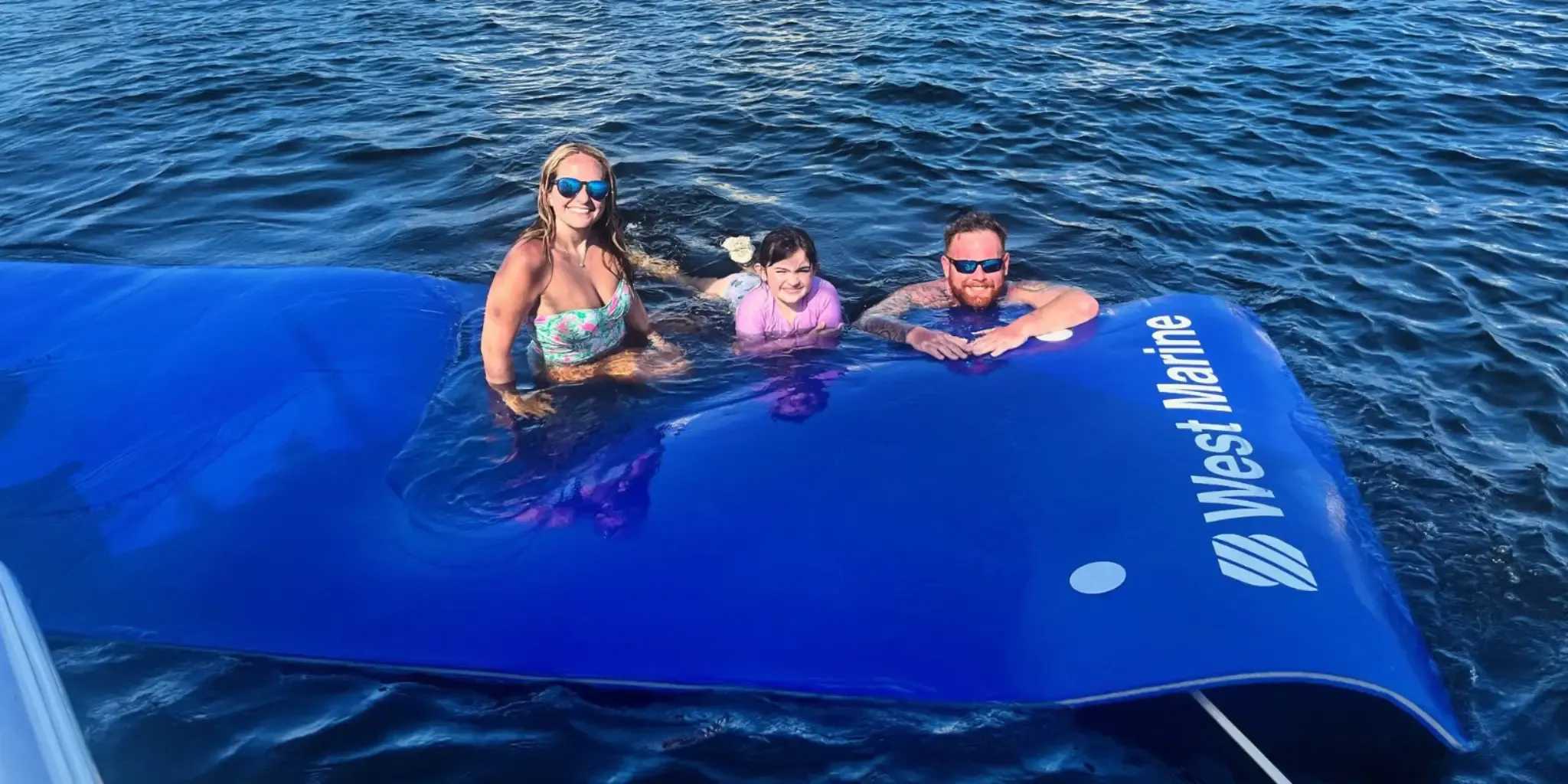 A family relaxing on a blue West Marine water mat in the ocean