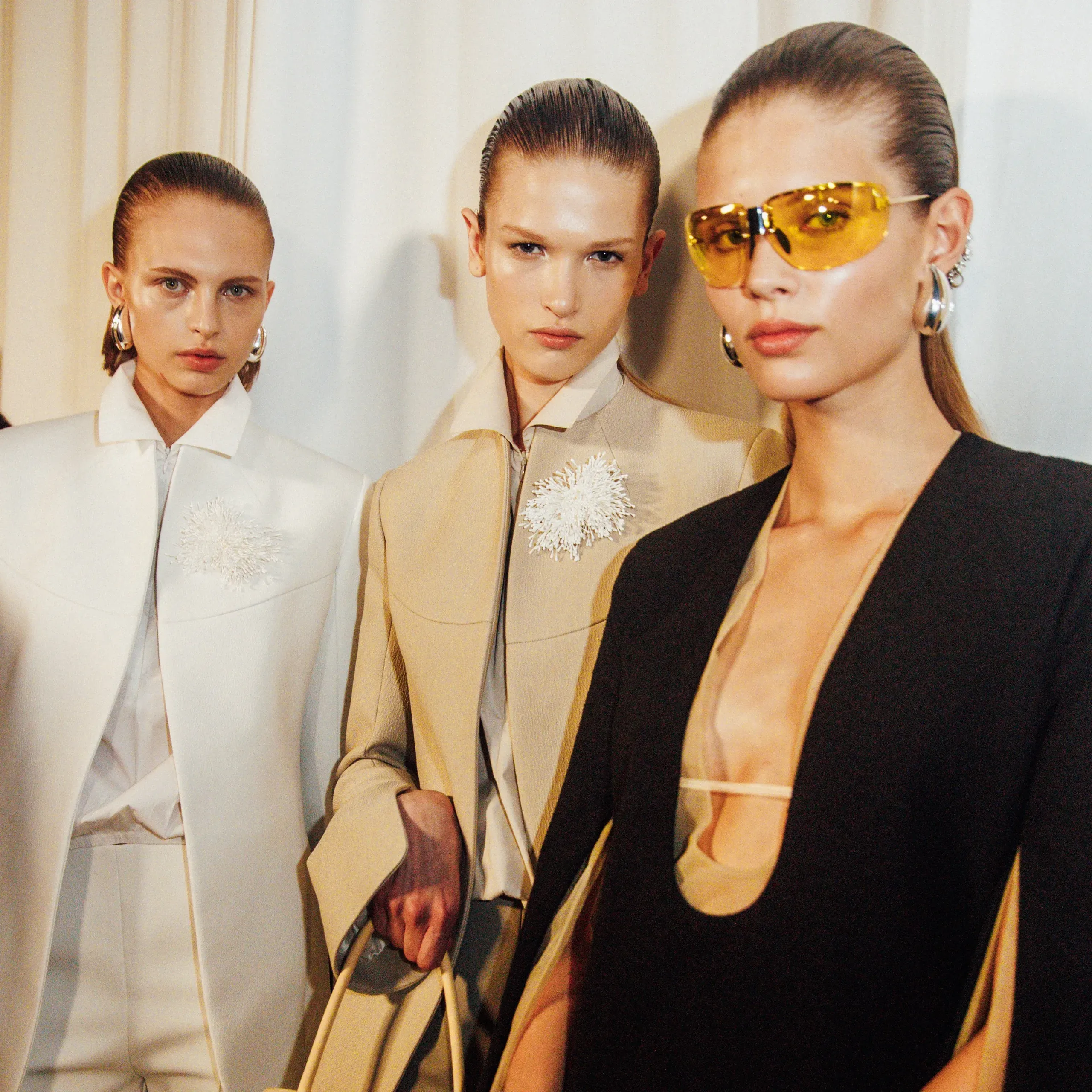 Three models in chic, structured outfits with bold accessories.